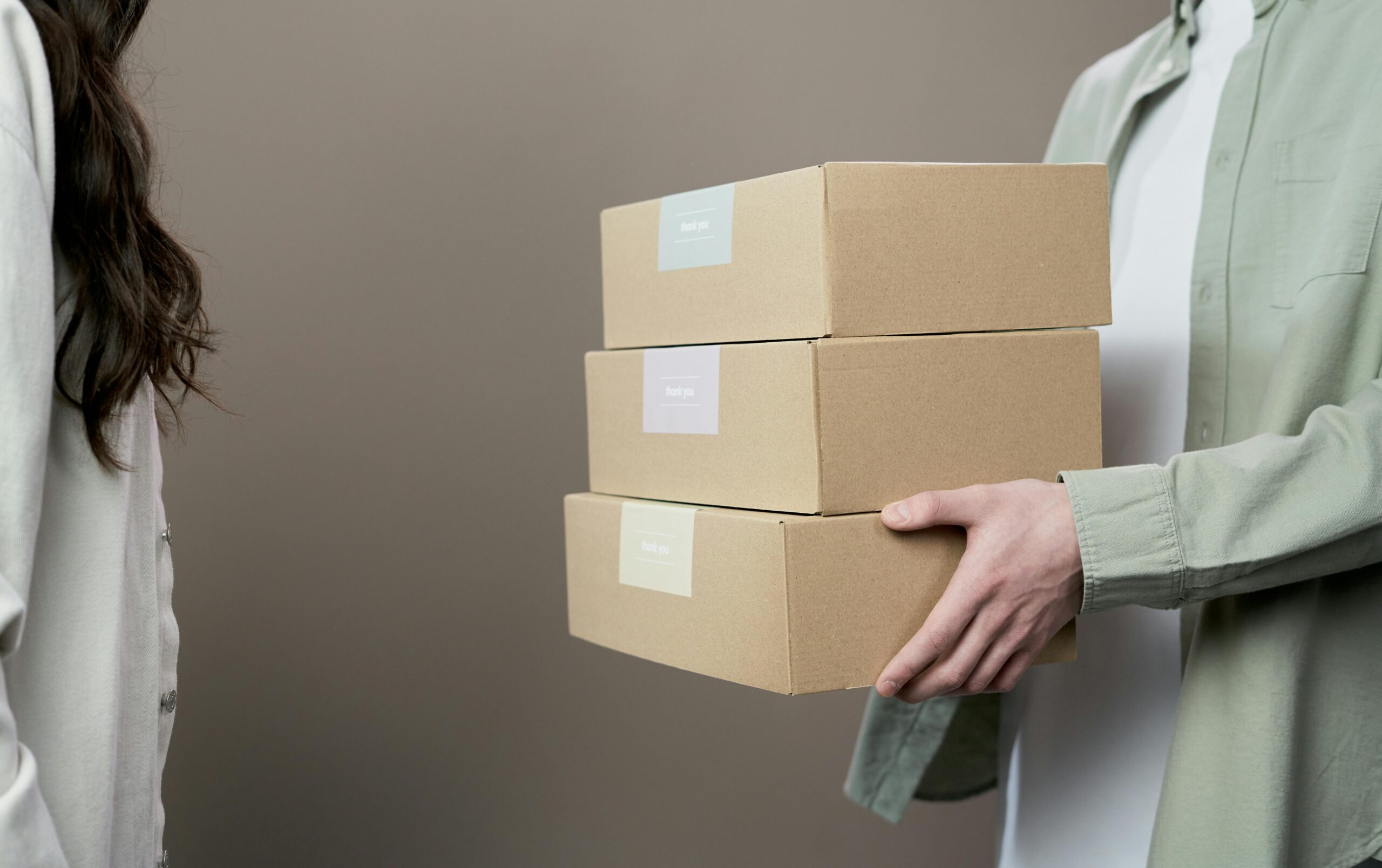 Two people exchanging stacked cardboard boxes against a neutral gray background in a studio setting.